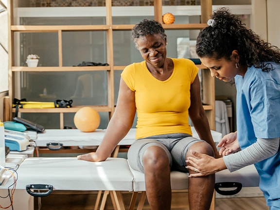 A medical professional bandages a woman's knee at a medbridge clinic.