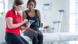 Physical therapist reviewing 2024 Physician Fee Schedule updates on tablet with patient in outpatient clinic setting.