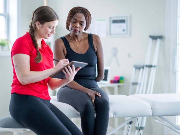 Physical therapist reviewing 2024 Physician Fee Schedule updates on tablet with patient in outpatient clinic setting.