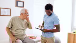 Clinician reviewing remote therapeutic monitoring (RTM) updates on tablet with older patient in outpatient clinic