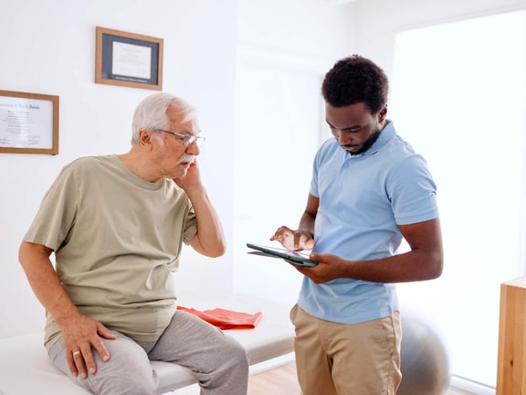 Clinician reviewing remote therapeutic monitoring (RTM) updates on tablet with older patient in outpatient clinic
