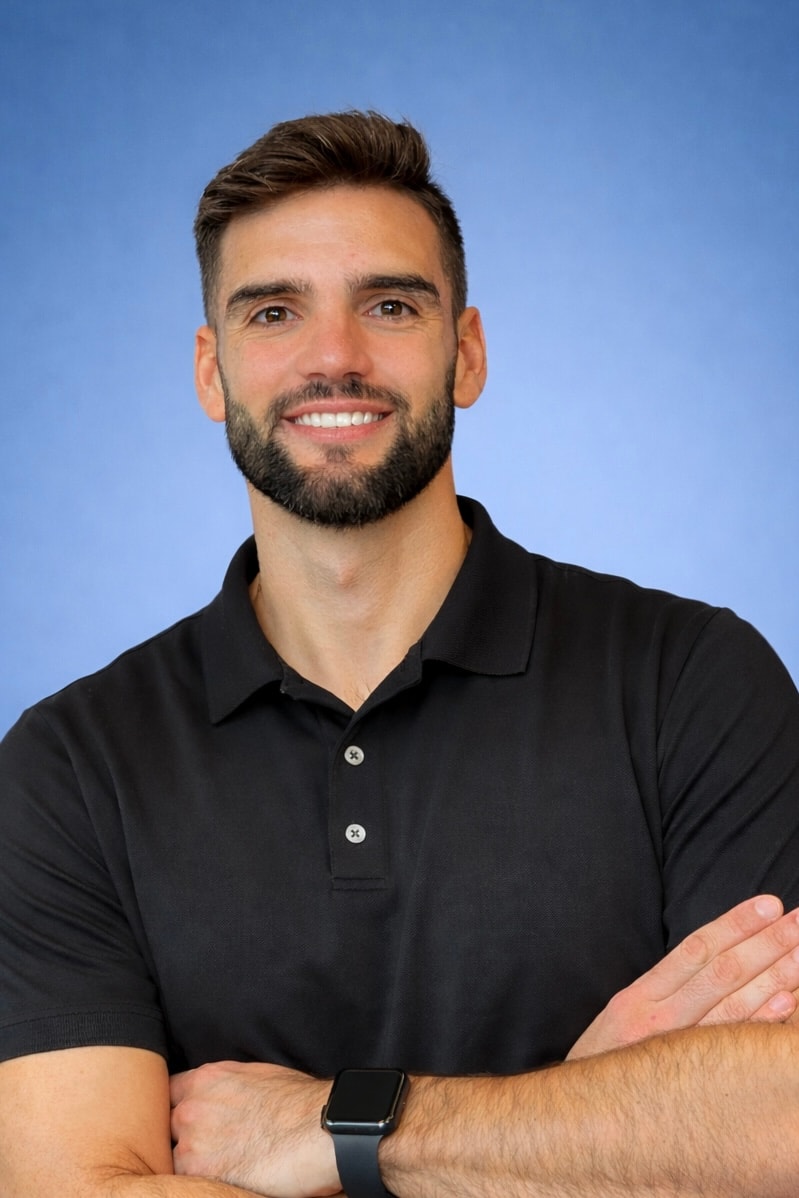 Man with short brown hair and beard in a black polo stands arms crossed on blue, representing medbridge healthcare software.