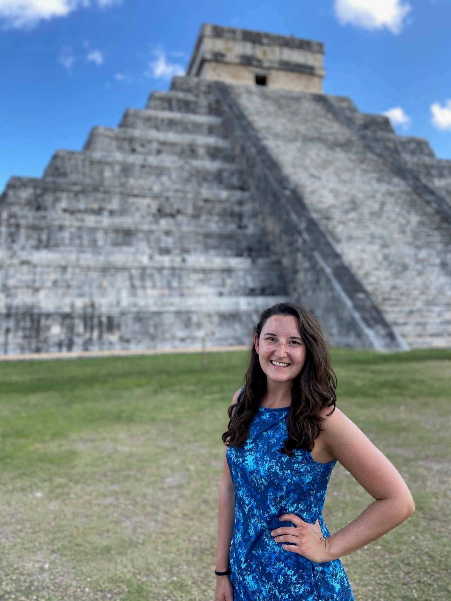 Smiling woman in a blue dress stands before Chichen Itza pyramid, after completing her medbridge healthcare education journey.