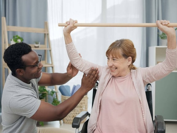 Therapist guiding a patient through a neuro rehab carryover shoulder mobility exercise with a dowel rod.