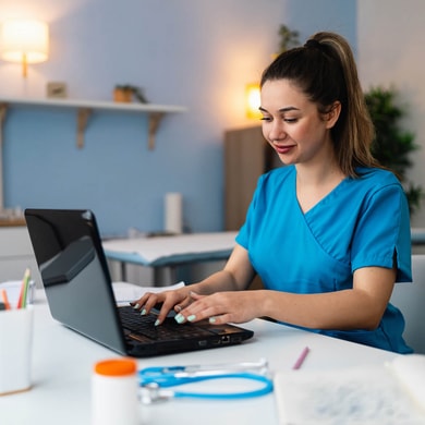 A healthcare professional in blue scrubs uses medbridge software on a laptop at a desk.