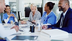 Diverse group of healthcare professionals smiling during a team meeting, symbolizing collaboration and anti-oppressive practice in healthcare.