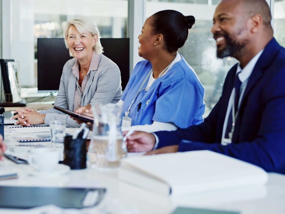 Diverse group of healthcare professionals smiling during a team meeting, symbolizing collaboration and anti-oppressive practice in healthcare.