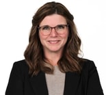 Smiling woman with glasses and brown hair in a black blazer, representing medbridge professionalism, on a white background.