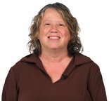 Woman with curly shoulder-length hair in a brown top smiles at the camera, showing confidence for medbridge digital healthcare.