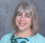 A woman with straight gray hair in a light blue sweater smiles at the camera, confident about digital healthcare innovations at medbridge.
