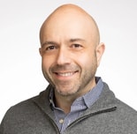 A bald man in a gray sweater over a checkered shirt smiles at the camera, representing medbridge professionalism.