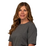 A woman with long wavy brown hair in a gray top stands against a white background, representing medbridge digital healthcare.