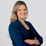 Smiling woman with long blonde hair in a blue blazer stands with arms crossed, representing medbridge and digital healthcare.