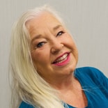Smiling older woman with long white hair and pink lipstick in teal top, representing positive digital healthcare impact for medbridge.