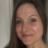 A woman with long brown hair and blue eyes smiles gently at the camera indoors, representing medbridge’s patient care approach.