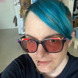 Person with teal hair, rainbow sunglasses, and lip piercing indoors, capturing a modern digital healthcare and medbridge vibe.