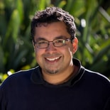 A smiling person wearing glasses and a black shirt stands amidst greenery, representing medbridge's dedication to lifelong learning in healthcare.