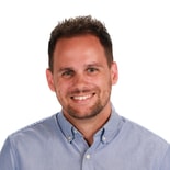 A smiling person with short hair and a beard wears a light blue button-up shirt against a white background, symbolizing medbridge's role in digital healthcare education.