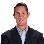 Man in a dark blazer smiles confidently, embodying expertise in healthcare education, against a white background.