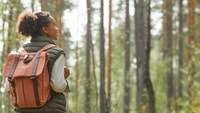 Individual with a backpack in a forest looking sideways at tall trees.