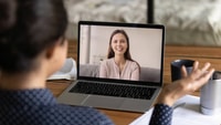 Person video calling a smiling woman on a laptop, with desk items visible.