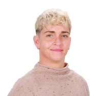 A smiling person with short curly blonde hair and earrings wears a light brown textured sweater, embodying the warmth of medbridge patient care software.