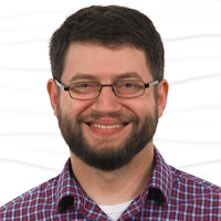A bearded person in glasses and a red plaid shirt smiles, symbolizing Medbridge's modern hybrid care.