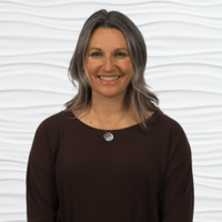 A woman in a dark top smiling warmly, representing compassionate care and innovative healthcare training for medbridge.