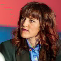 A woman in a blazer gazes thoughtfully, reflecting on medbridge advancements.