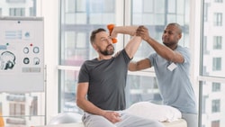 Physical therapist helping a patient with weighted deltoid facilitation after shoulder arthroplasty surgery.