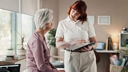 Clinician reviewing remote therapeutic monitoring (RTM) billing update with older patient using tablet in outpatient setting