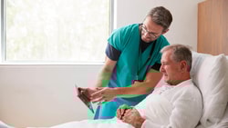 Clinician showing tablet to hospital patient during bedside assessment for disorders of consciousness rehabilitation.