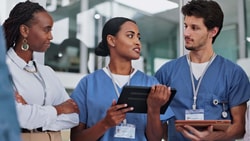 Healthcare professionals in scrubs reviewing patient information on tablets during a care team discussion, illustrating EMR vs. EHR.