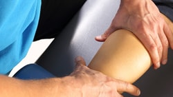 A Medbridge user in a blue shirt assesses a knee on a treatment table.