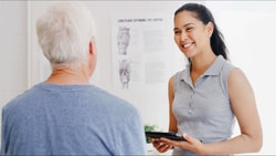 Clinician discussing remote therapeutic monitoring (RTM) and reimbursement updates with older patient in clinic