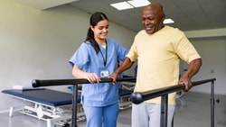 Physical therapist assisting patient with gait training on parallel bars in outpatient rehabilitation clinic