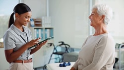 Clinician using remote therapeutic monitoring (RTM) tablet with older patient during outpatient rehabilitation visit