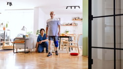 Physical therapist supporting intentional neuro rehab mobility training during balance and gait exercises at home.