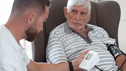 Home health clinician uses a blood pressure monitor while discussing heart failure care with an older male patient.