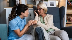 Clinician kneeling beside an older adult, offering calm support during a moment of distress in dementia care.