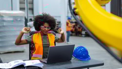 Person wearing safety gear while working on a laptop at a desk. Risk adjustment factor.