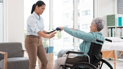 Physical therapist supporting seated balance and posture in an older adult with mobility limitations during rehabilitation care.