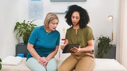 A healthcare worker shows medbridge info on a tablet to an older woman in a medical office.
