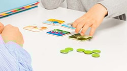 Two individuals organize picture cards and tokens on a table near a Medbridge book.