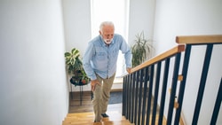 Older adult using stair railing at home while managing knee pain, illustrating fall risk scenarios addressed with the ABC Scale PDF.