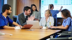 Healthcare team and analyst reviewing data dashboards in a meeting, discussing value-based care analytics strategies.