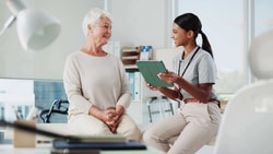 Clinician using tablet to discuss remote therapeutic monitoring with an older patient during a clinic visit.