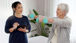Physical therapist guides older patient using dumbbells during exercise, demonstrating technology-supported physical therapy care