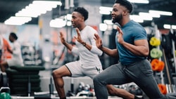 Athletes performing lunges during return-to-sport strength training session in a gym.