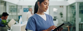 A healthcare worker in scrubs uses a tablet with medbridge software in a bright clinic, with staff in the background.